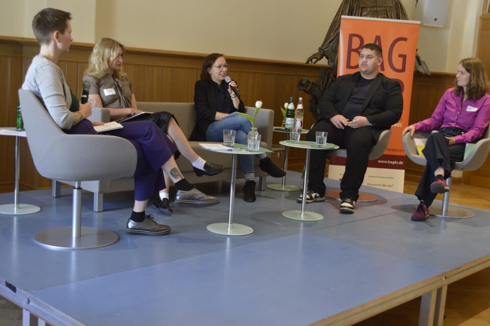 Podiumsdiskussion beim BAGKR-Jahrestreffen im Paul-Gerhardt-Stift: fünf Teilnehmende auf Stühlen, Mikrofon, Banner, Gläser